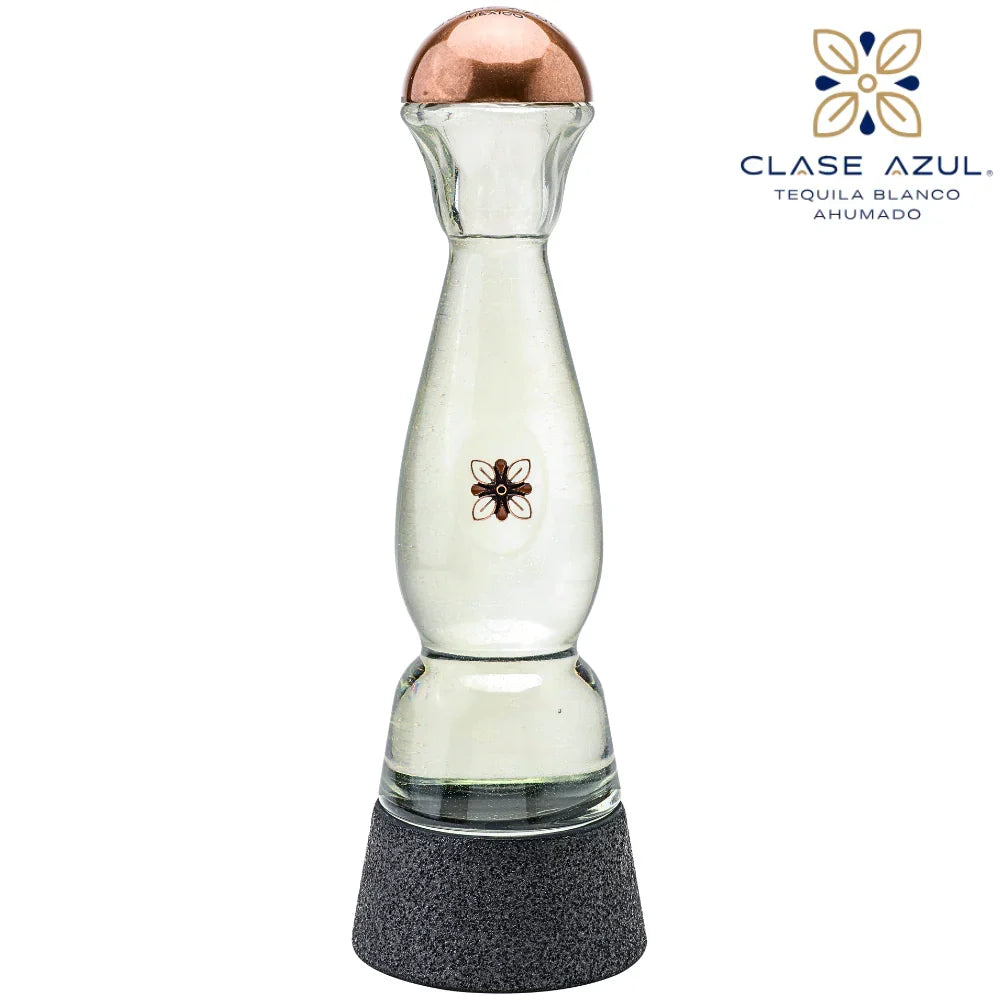 A clear glass tequila decanter with a copper-colored top, a small black floral emblem on the front, and a textured dark gray base. The Clase Azul logo is visible in the upper right corner against a plain white background.